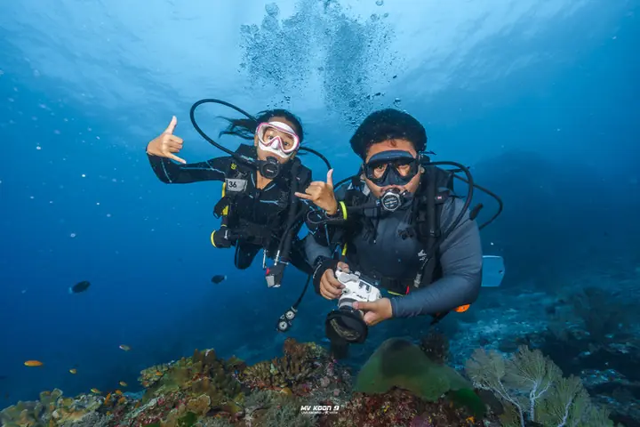 Two smiling divers giving a thumbs-up underwater